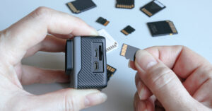 Action camera and microSD memory card in hands on the back of other SD memory cards. Background from gadgets and digital devices.